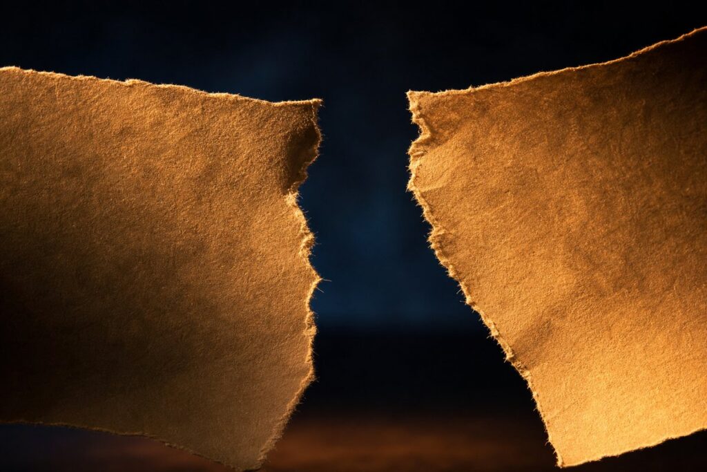Two torn pieces of brown paper with jagged edges on dark background representing CBSE answer sheet mismatch controversy