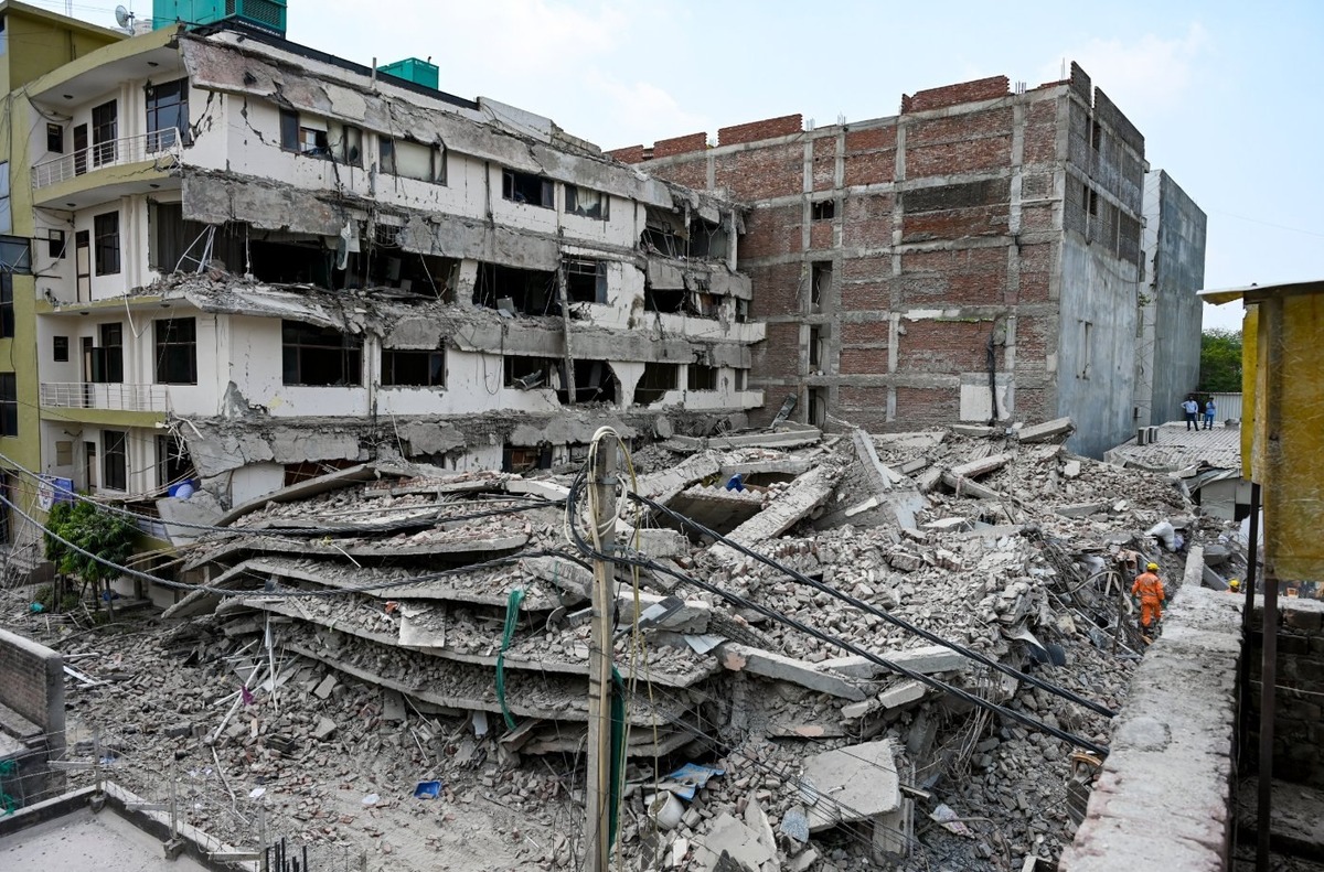 Pancaked floors and rubble of a collapsed five-storey building in Saidulajab near Saket Metro, Delhi, with an orange-clad rescue worker searching debris, May 30 2026